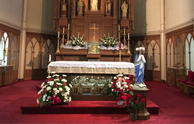 Mary, crowned in May, stands in front of the altar.